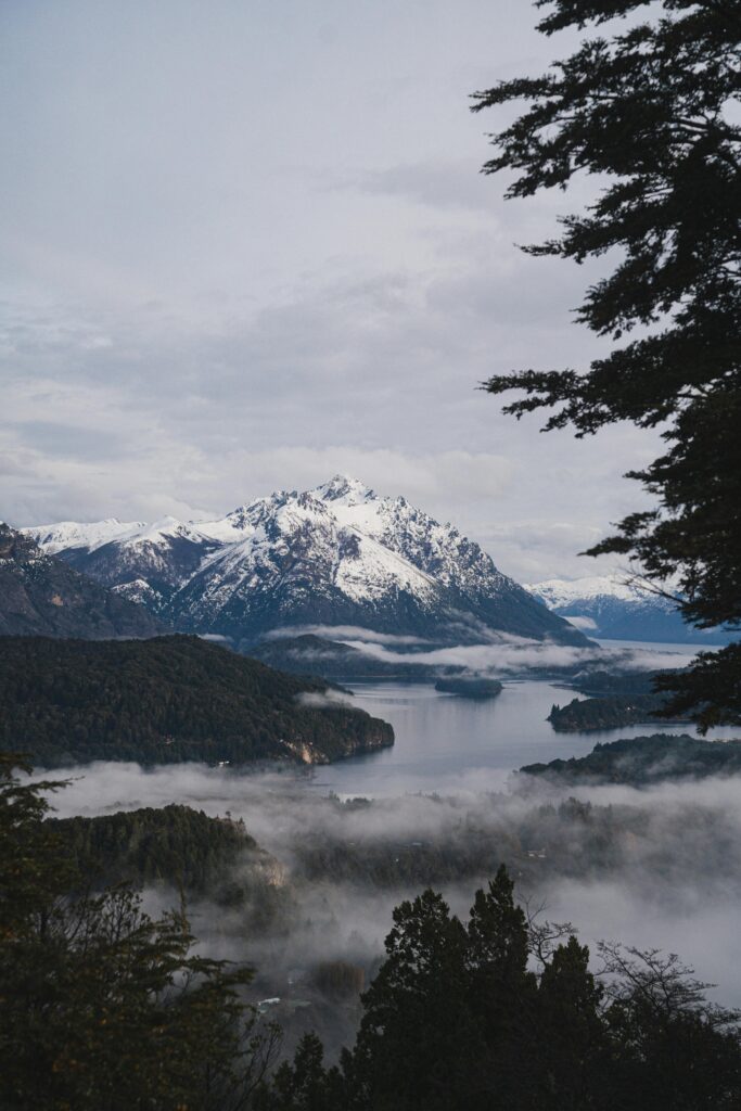 Scenic aerial view of snow-capped mountains reflecting over a misty lake in Bariloche, Argentina.