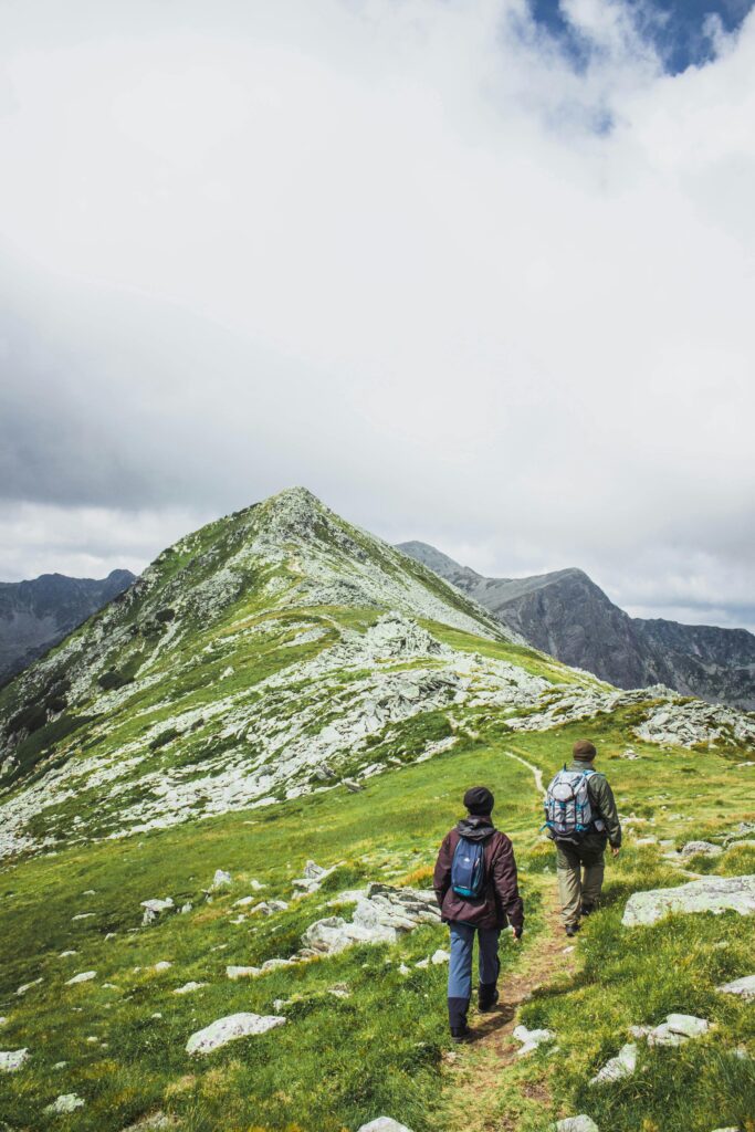 Two hikers trekking a scenic mountain trail in Romania under a dramatic sky.